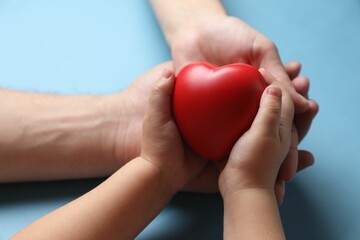 Sticker - Father and his child holding red decorative heart on light blue background, closeup