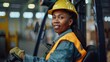 African American woman in safety gear driving - A confident African American woman wears a safety helmet while operating a forklift in an industrial setting