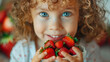 Close-up of a smiling curly-haired child with blue eyes holding ripe strawberries
