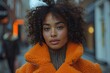 Black woman with afro curly hair wearing vivid coat standing on street with blurred background