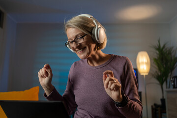 Poster - Happy mature woman listening to music through wireless headphones at home