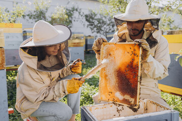 Couple of happy smiling beekeepers working with beekeeping tools near beehive at bee farm