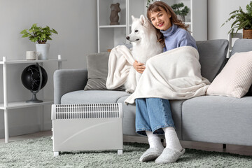 Sticker - Young woman with Samoyed dog and plaid on sofa warming near radiator at home