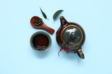 Wall Mural - Teapot, cup of hot tea and spoon with dry leaves on blue background