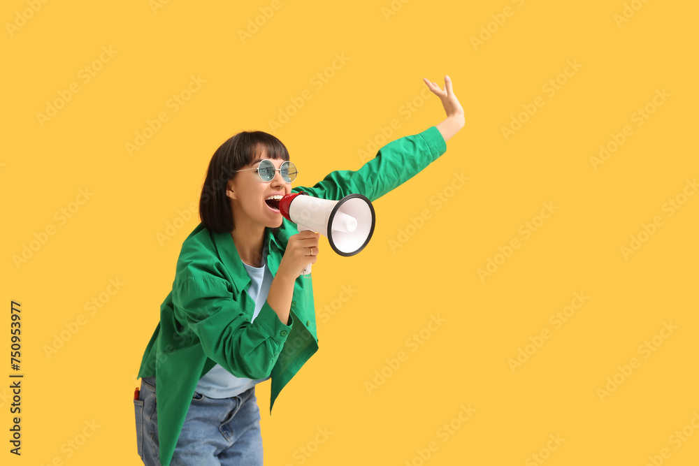 Screaming young woman with megaphone  on yellow background