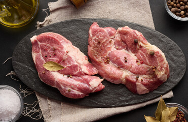 Wall Mural - Two raw pork neck steaks on a board and spices for cooking. Top view