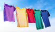 Different t-shirts drying on washing line against blue sky, banner design