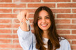 © simona - Happy woman holding keys to new home, looking at camera and smiling. Portrait of first time buyer, house owner, apartment renter, flat tenant or landlady. Moving day and buying own property concept