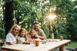 © Zamrznuti tonovi - A happy family sitting at table in nature and looking at the camera.