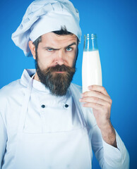 Dairy farmer products. Professional male chef in white apron with glass bottle of milk. Serious bearded cook in chef hat and uniform with bottle of kefir, yogurt or milkshake. Organic healthy food.