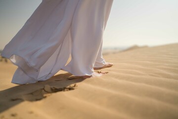 Close up woman wearing white abaya walking in the desert sand
