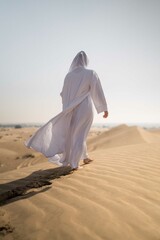Wall Mural - Arabic woman wearing white abaya in the desert
