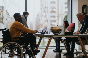 Wall Mural - Inclusive work culture depicted with multi-ethnic team including a person with a disability engaging in a collaborative work session in a bright office.