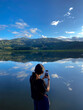© Luis Herrera/Stocksy - travel woman using her phone by a lake