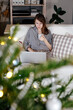 © Sergey Narevskih/Stocksy - Female on couch using laptop near Christmas tree