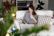 © Sergey Narevskih/Stocksy - Woman spending time on couch using laptop on Christmas holiday
