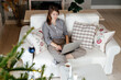 © Sergey Narevskih/Stocksy - Woman sitting on couch using laptop near Christmas tree at home