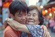 Asian Teenage son hugging his senior mother outside in town when spending time together
