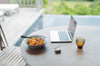 © Marc Tran/Stocksy - Open laptop and pasta in a plate on wooden table on the patio at home