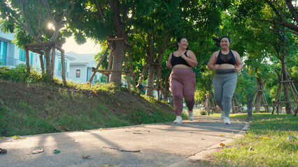 Two asian woman fat in sportswear jogging together on pathway at park, woman and friends obesity doing activity with cardio or running, workout and exercise, plus size and health for weightloss.