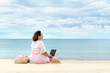 © Marc Tran/Stocksy - A woman using laptop computer while sitting on the beach