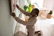 © Milles Studio/Stocksy - Black lady attaching framed image to wall