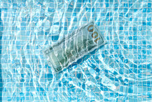 100 dollar bill sinking in swimming pool water with gentle rippl