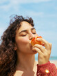 © ohlamour studio/Stocksy - Woman biting a peach with pleasure expression at the beach