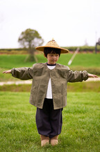 Little Asian Boy Imitating A Scarecrow Wearing A Straw Hat Outdoors