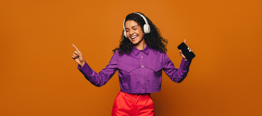 Wall Mural - Cheerful woman celebrating with vibrant moves and music on orange background