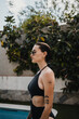 © Susana Ramírez/Stocksy - Portrait of woman in swimsuit in a garden with swimming pool