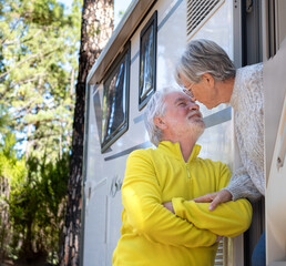 Wall Mural - Smiling senior couple outside their camper van motor home exchange kisses enjoying retirement lifestyle. Elderly people and freedom vacation travel in the forest.