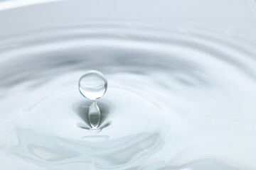 Splash of clear water with drop on light grey background, closeup