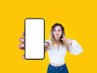 Beautiful woman smiling with braces, holding big mobile cell phone close up to camera. Pointing finger and looking empty blank white screen smartphone mock up. Advertisement concept idea.
