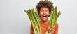 Young woman with short curly hair revels in joy of healthy eating holds asparagus stalks highlights pleasure of eating organic food exclaims loudly isolated on white wall. Nutrition and wellbeing