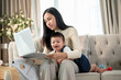 © bongkarn - A happy Asian businesswoman mom is working from home and taking care of her naughty baby boy.