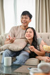© bongkarn - A happy young Asian couple is relaxing on a sofa, enjoying watching television together at home.