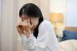 © bongkarn - A young Asian woman in pajamas is feeling sad and depressed, crying alone in her bedroom.