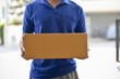 © bongkarn - A cropped shot of a delivery man in a blue shirt holding a cardboard box in front of the door.