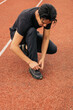 © Daniel Zapata/Stocksy - Man on a jogging track tying his shoelaces.