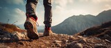 Fototapeta  - A hiker is seen carefully traversing rugged terrain, making their way up a hill on a bright and sunny day. The focus is on their feet as they take each step upwards.