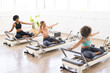 © Wavebreak Media - Young Caucasian woman and biracial women exercising on Pilates reformers in a bright studio