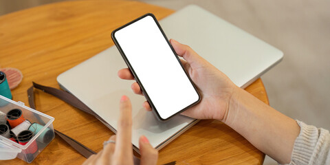 Wall Mural - Mockup smartphone of a woman holding and using mobile phone with blank screen while on the sofa with feeling relaxed