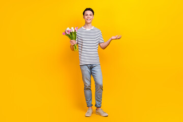 Canvas Print - Full size photo of nice student dressed striped t-shirt hold tulips palm presenting promo empty space isolated on yellow color background