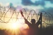 a person raising their arms up behind a barbed wire fence