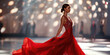 A model in a flowing red gown captivatingly walks the runway under bright stage lights.