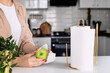 Woman wiping green apple with paper towel in kitchen, closeup
