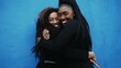 African American Adolescent daughter hugs mother in genuine affectionate love. Caring moment between parent and offspring on blue urban wall. Love and affection