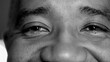 Macro close-up of a senior middle-aged man eyes with wrinkles and mouth smiling, person of African descent feeling happy