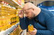 Shocked overweight man raising his glasses to his forehead and looking on price of vegetable oil in supermarket. Amazed male by food inflation and rising prices on sunflower oil in grocery store